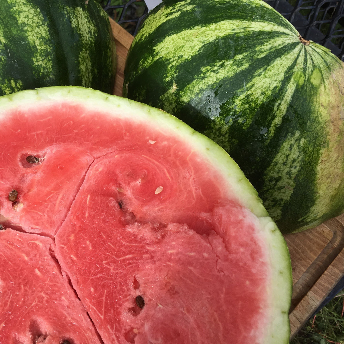 Gros plan de deux Melons d&#39;Eau Sweet Dakota Rose de Tourne-Sol à l&#39;écorce rayée de vert et dont un coupé en deux, révélant sa chair rose et sucrée parsemée de graines, reposant élégamment sur une surface en bois.