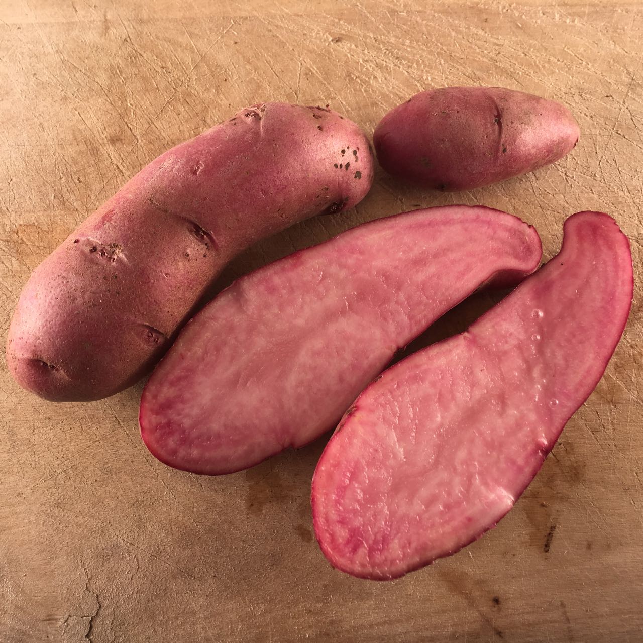 Deux pommes de terre semence Amarosa TS entières et une tranchée, révélant leur intérieur rosé, reposent sur une surface en bois comme des pommes de terre biologiques fraîches.